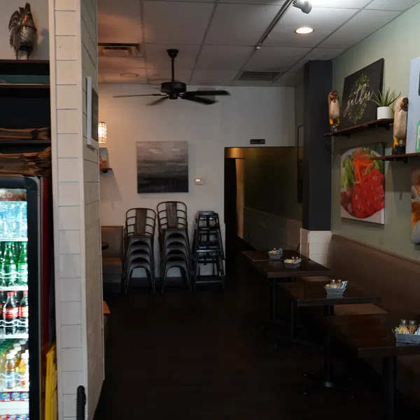 Cozy cafe interior with stacked chairs, wall art, cushioned bench seating, and a refrigerated display of beverages.