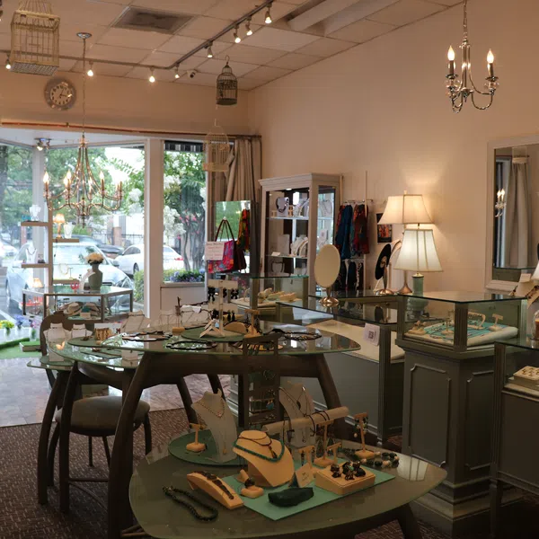 Interior of a jewelry store with display cases, necklaces, lamps, mirrors, and a large window showing parked cars.