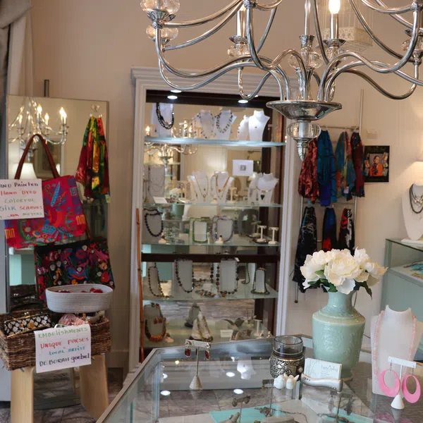 Bright boutique interior with glass jewelry displays, colorful scarves, and decorative flowers in a vase.