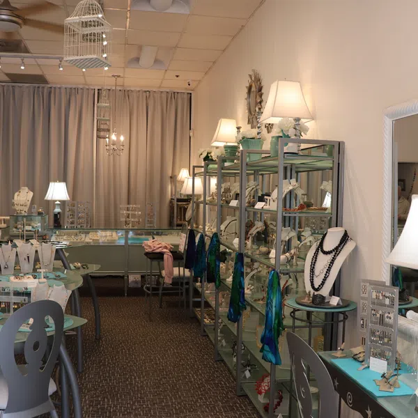 Interior of jewelry store with necklaces, rings, earrings displayed on tables and shelves under warm lighting.