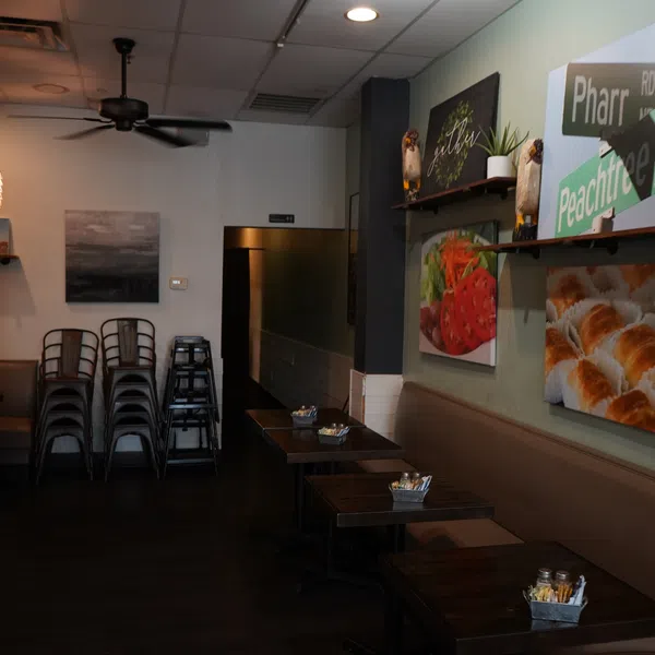 Cozy empty cafe interior with stacked chairs, dark wooden tables, ceiling fan, and food-themed wall art.