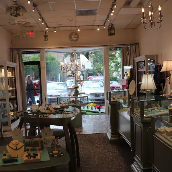 Interior of a cozy jewelry store with display cases, chandeliers, and various jewelry pieces on tables and shelves.