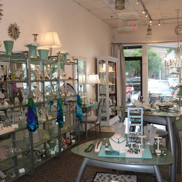 Bright jewelry store interior with glass display shelves, tables showcasing necklaces, rings, and decorative lamps.