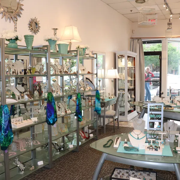 Bright jewelry store with glass displays showcasing necklaces, bracelets, rings, lamps, and decorative scarves.