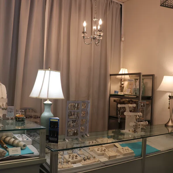 Jewelry store display with necklaces, earrings, rings, lamps, and a chandelier on beige walls and curtains.