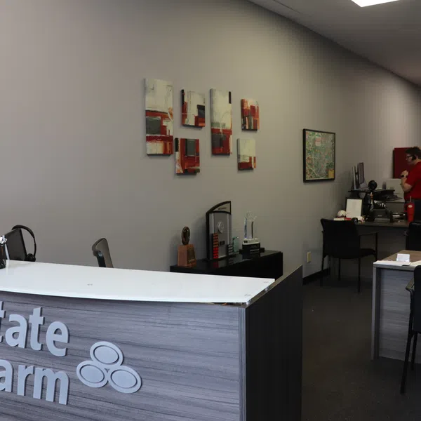 Modern State Farm office reception with decor, desks, and employees working in the background under bright lighting.
