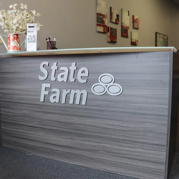 Modern State Farm office reception desk with logo, flower vase, brochures, and wall art in a professional setting.