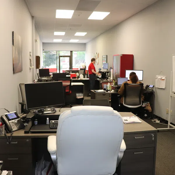 Modern office space with desks, computers, whiteboard, and employees working in an open layout under fluorescent lighting