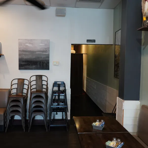 Cozy restaurant interior with stacked metal chairs, dark wooden tables, and vibrant food artwork on the walls.