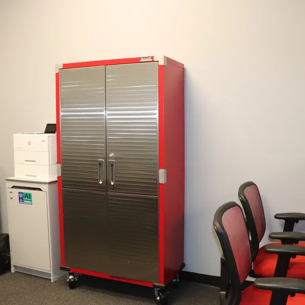 Red and silver metal storage cabinet in office room with chairs, desks, and computer monitors around it.