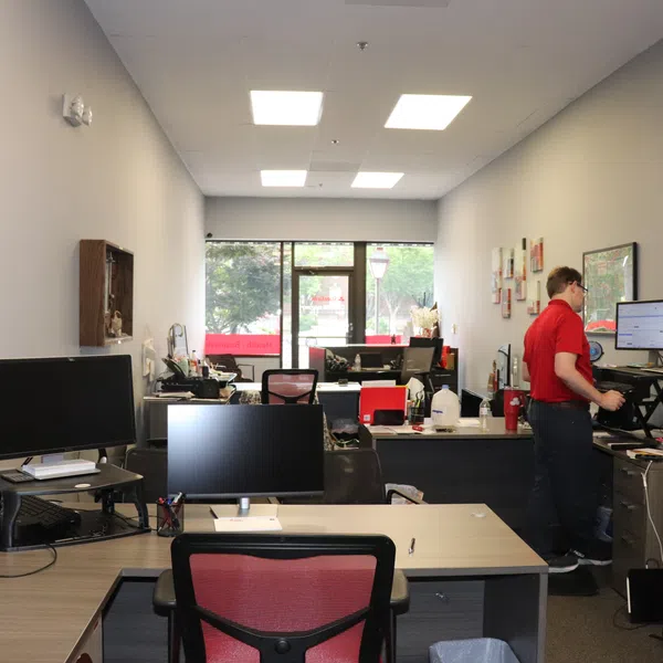 Modern office space with multiple desks, computers, and a man working on a standing desk near the window.