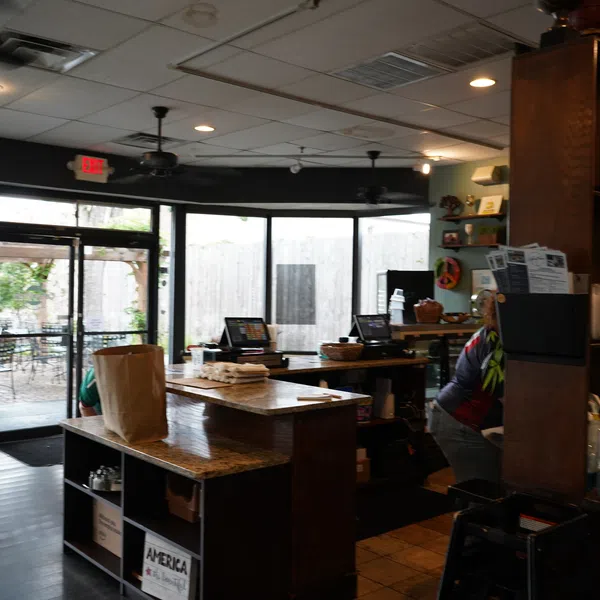 Interior of a cozy cafe with wooden counters, glass doors, and outdoor seating visible through windows.