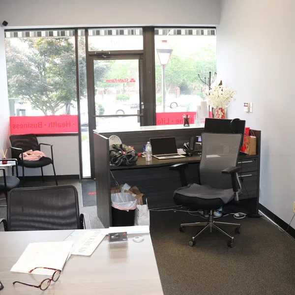 Modern office reception area with desk, chairs, laptop, paperwork, and large glass door letting in natural light.