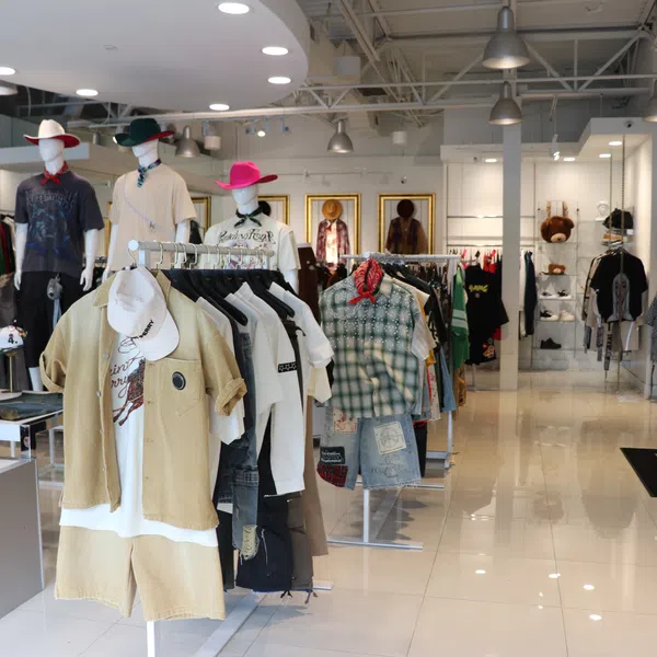 Modern clothing store interior with mannequins dressed in casual outfits and racks of apparel under bright lighting.