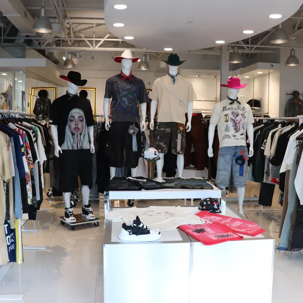 Modern clothing store interior with mannequins in casual wear and cowboy hats, racks of clothes, and display tables.