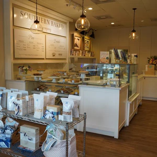 Cozy bakery interior with glass display cases of pies, wooden floors, hanging lights, and packaged goods on metal shelves