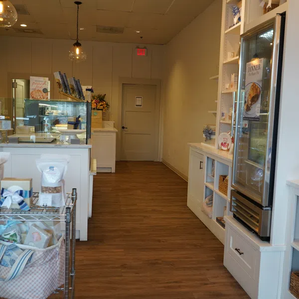Interior of a cozy bakery with wooden floors, display cases, shelves with products, and warm lighting.