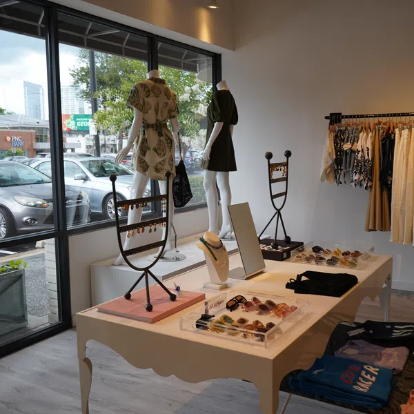 Boutique clothing store interior with mannequins, dresses, accessories, and large front windows showing parked cars.