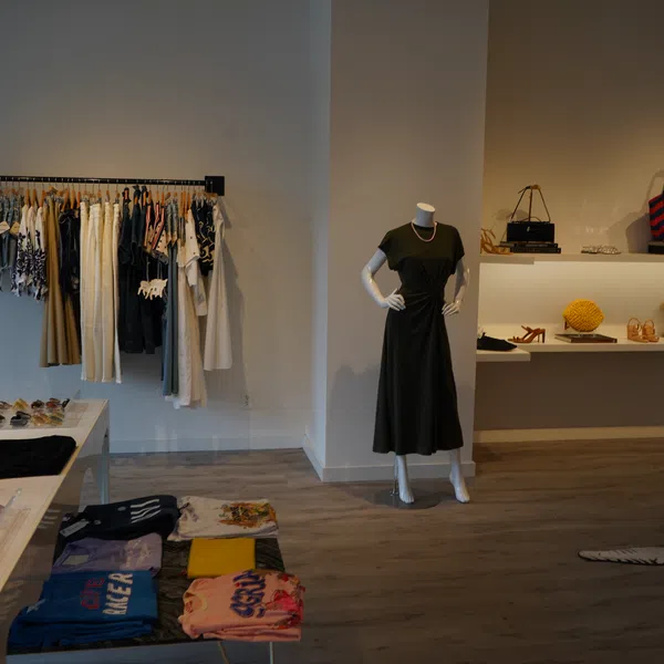 Modern boutique interior with clothing rack, mannequin in black dress, shelves with bags and accessories.