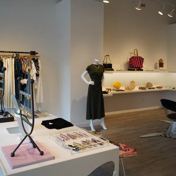 Modern boutique interior featuring clothing racks, accessories display, mannequin with black dress, and seating area.