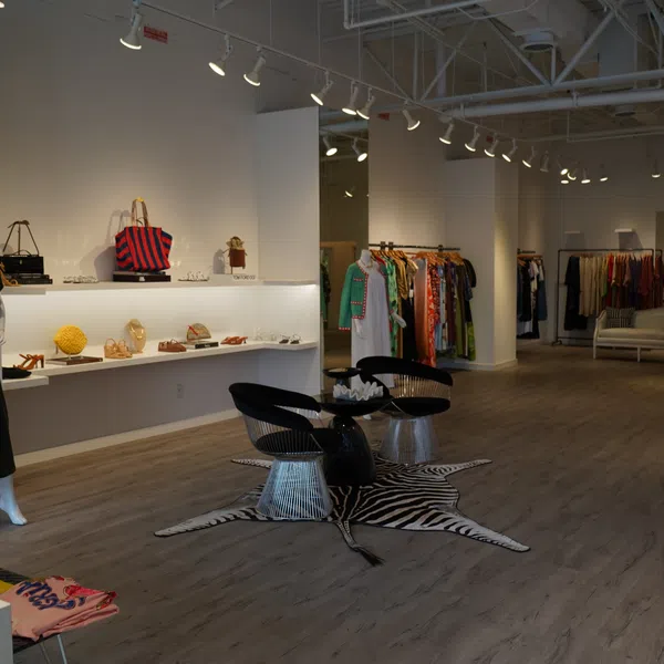 Interior of a modern clothing boutique with dresses, handbags, and seating area on a zebra rug under track lighting.