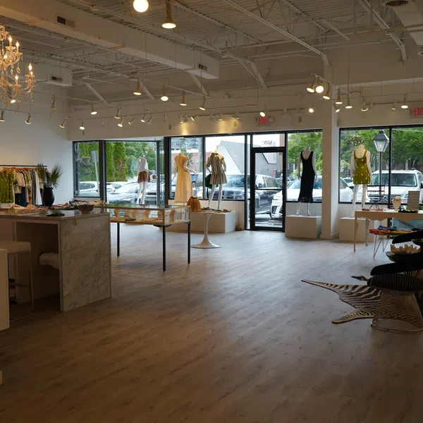 Bright boutique interior with mannequins displaying dresses, clothing racks, modern furniture, and large front windows.