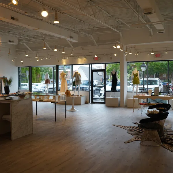Spacious modern clothing store with mannequins, large windows, hardwood floors, and elegant lighting fixtures.