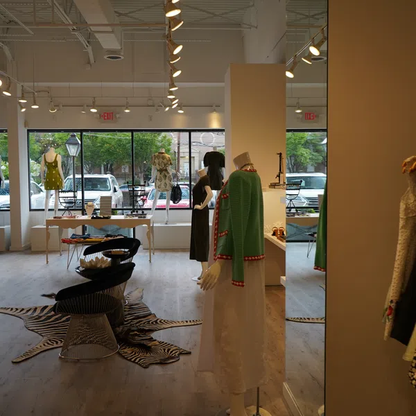 Modern boutique interior with mannequins, contemporary furniture, clothing racks, and large storefront windows.