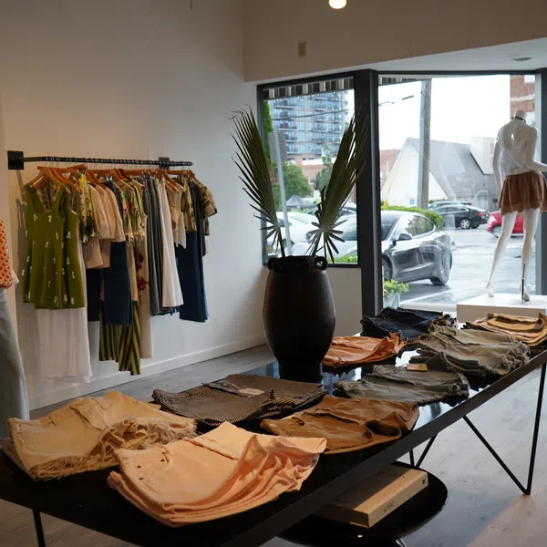 Modern boutique clothing store with casual wear displayed on table, rack, and mannequins by large windows.