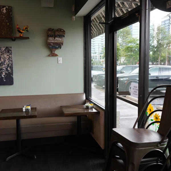 Cozy café corner with cushioned bench, wooden tables, stacked chairs, and large windows overlooking rainy street.