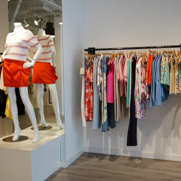 Bright clothing store interior with mannequins and colorful garments hanging on racks against white walls.