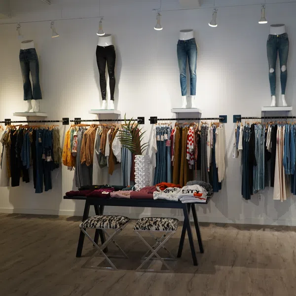 Modern clothing store interior with mannequins, hanging clothes, folded apparel, and seating area under soft lighting