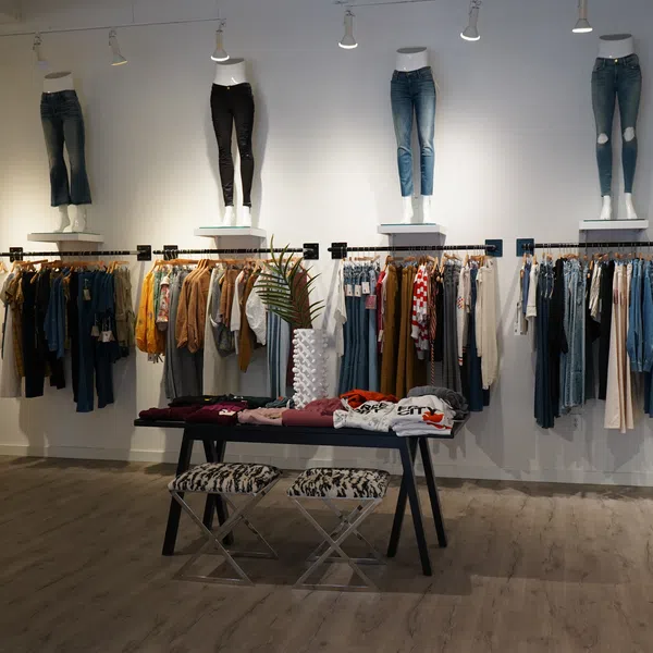 Modern boutique interior with clothing racks, mannequins displaying jeans, folded apparel on table, and stylish decor.
