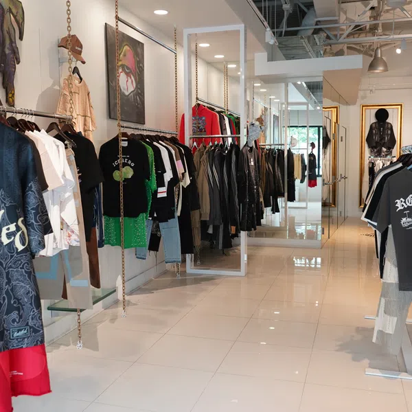 Modern clothing store interior with hanging shirts, jackets, and streetwear displayed on white tile floor.