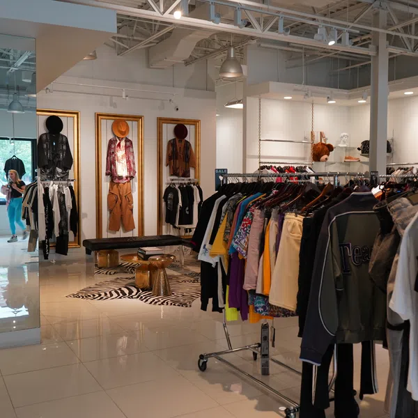 Modern clothing store interior with racks of colorful apparel and mannequins against white walls and tiled floor.