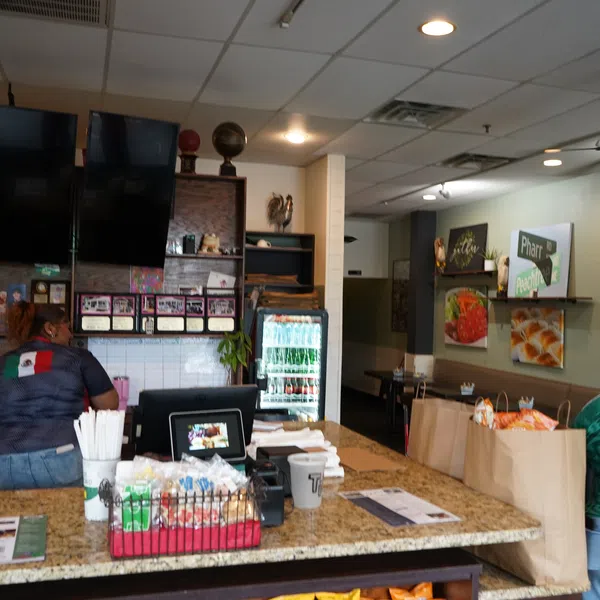 Interior of a casual restaurant with two workers behind the counter and takeout bags on the table.