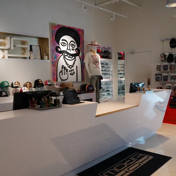 Modern retail store interior with white counters, mannequins, hats, sunglasses, and vibrant wall art.