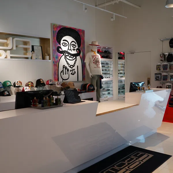 Modern retail store interior with white counters, hats on display, mannequins, and colorful graffiti artwork on wall.
