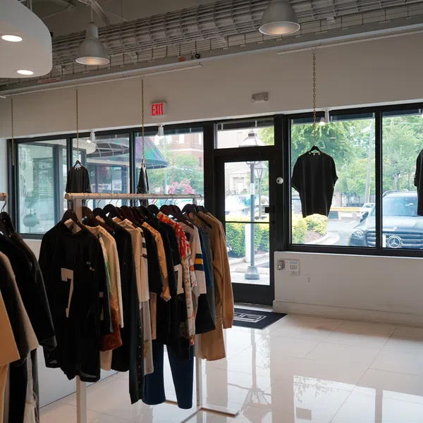 Interior of a clothing store with racks of shirts and jackets displayed near large windows and glass doors.