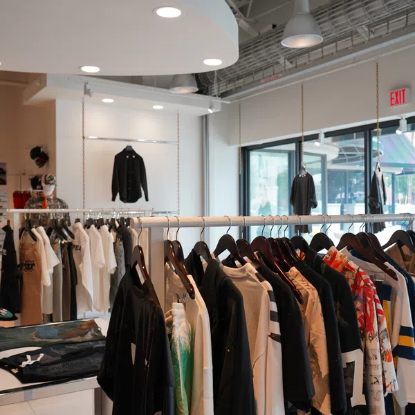 Modern clothing store interior with racks of shirts, jackets, and casual wear under bright ceiling lights.