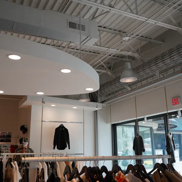Modern clothing store interior with hanging racks displaying jackets and shirts under industrial ceiling lighting.