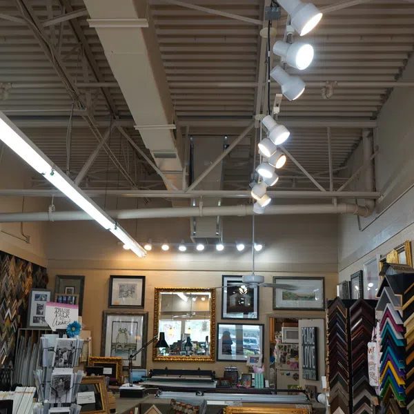 Interior of a frame shop with various picture frames, artwork, mirrors, and bright overhead lighting