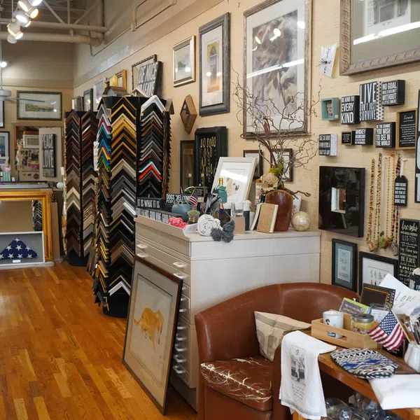 Interior of a custom framing and gift shop with artwork, picture frames, and decorative signs on display.