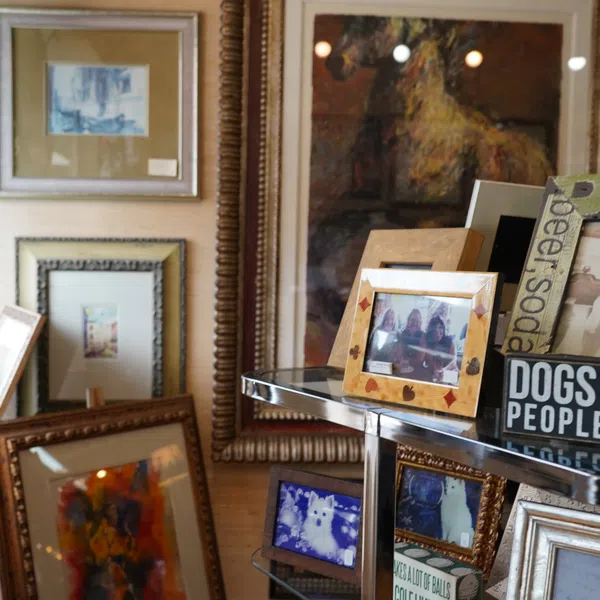 Interior display featuring framed photos, art prints, wine bottles, and decorative signs on shelves and walls.