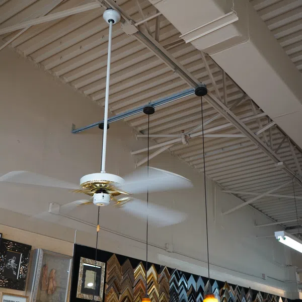 White and gold ceiling fan spinning in industrial space with pendant lights and framed art on wall below