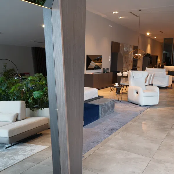Modern living room interior with white sofas, armchairs, plants, and warm lighting on tiled floor.