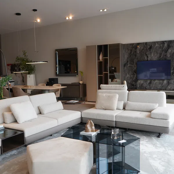 Modern living room with beige sectional sofa, glass coffee tables, indoor plants, and wall-mounted TV on textured stone wall.