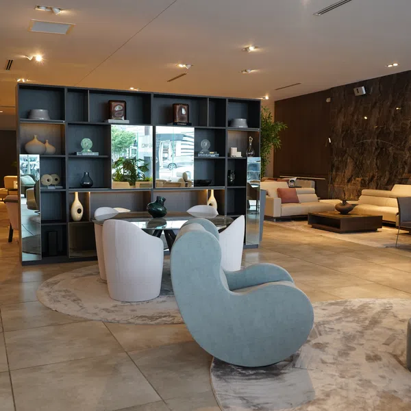 Modern open living room with diverse seating, decorative shelves, marble wall, and neutral tiled flooring