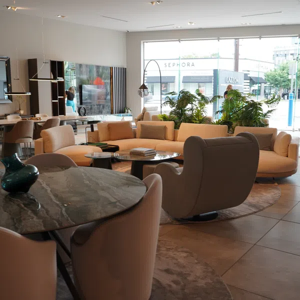 Modern living room with beige sectional sofa, armchairs, marble-top table, and large windows with natural light.