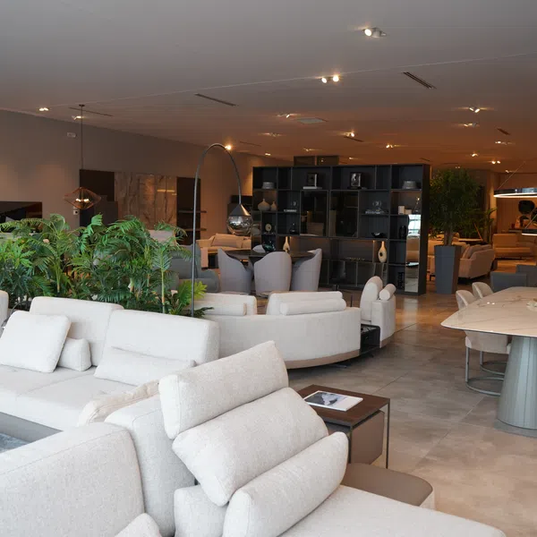 Modern furniture showroom with white sofas, dining table, green plants, and ambient lighting